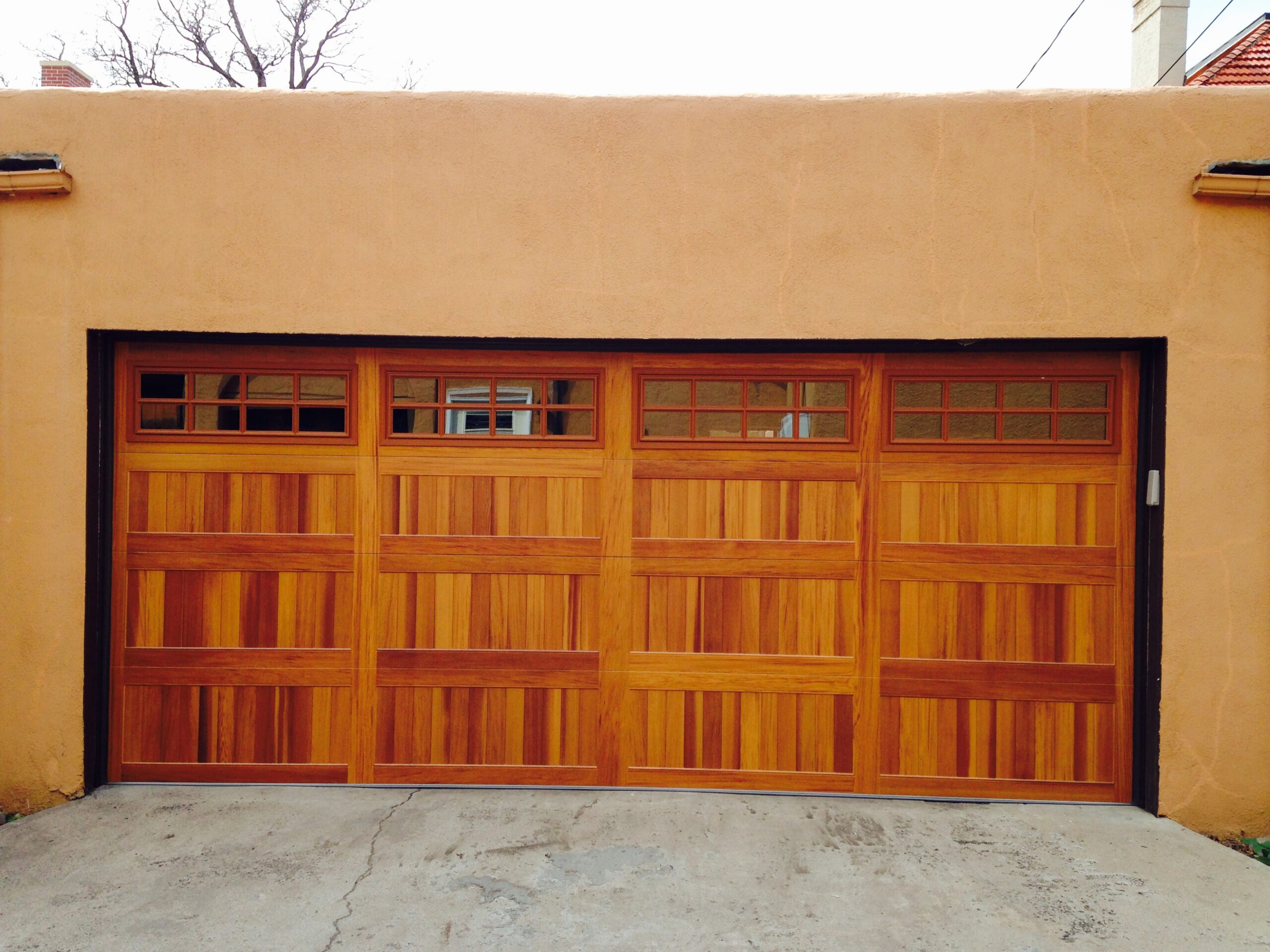 After: Custom Wood-Tone Carriage Style Garage Door Upgrade with Divided Lite Windows on Southwestern Stucco Home